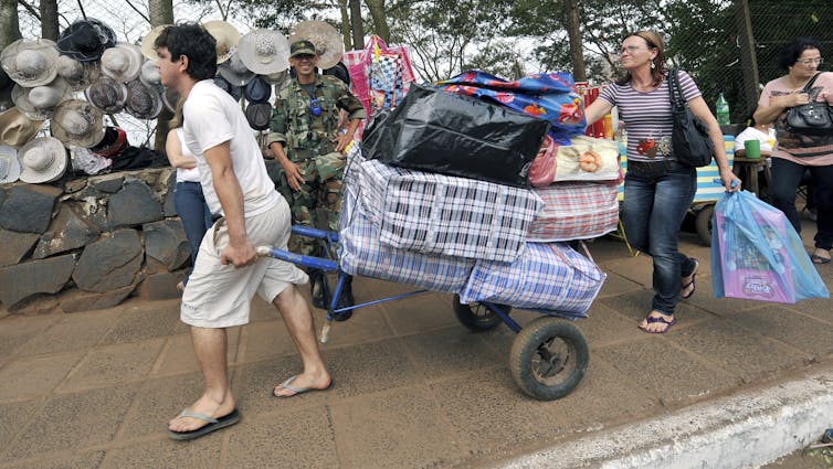 People lug large amounts of stuff in huge, colorful bags.