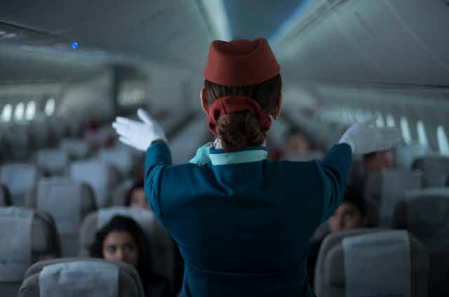 A flight attendant wearing gloves points down the plane.