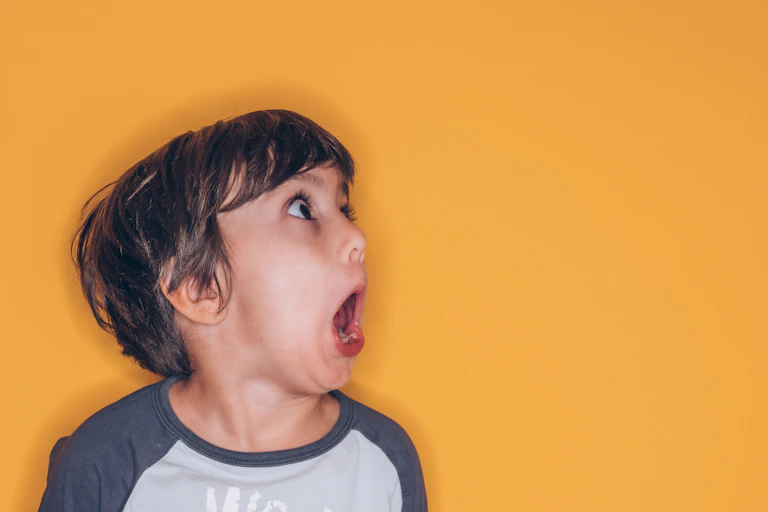 A young child makes a silly expression with open mouth and wide open eyes.