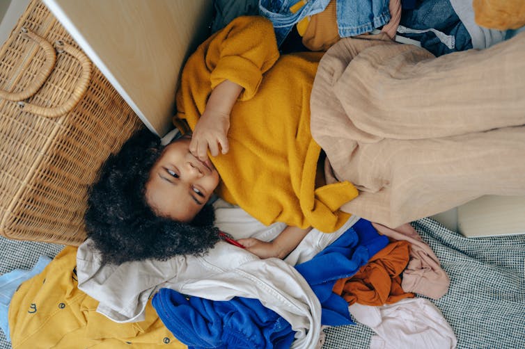 A child lies on the floor on a pile of clothes.