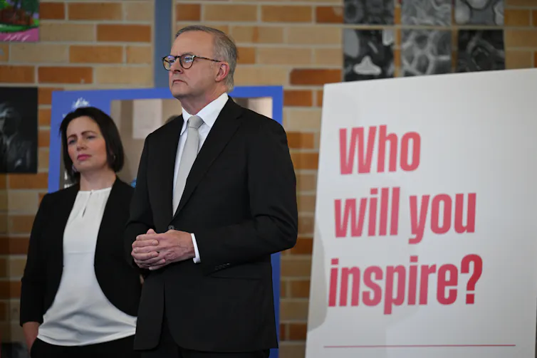 Prime Minister Anthony Albanese stands in front of a sign that says 'Who will you inspire?'