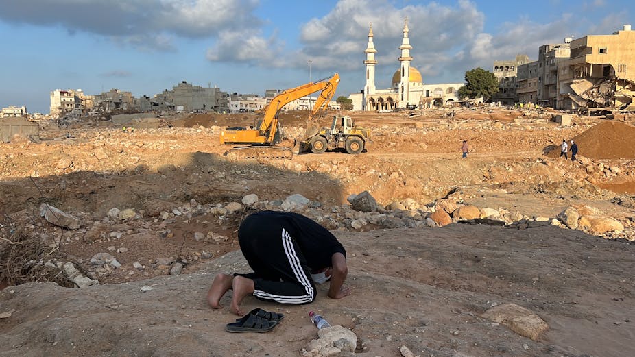 A man prays on his knees amid rubble.