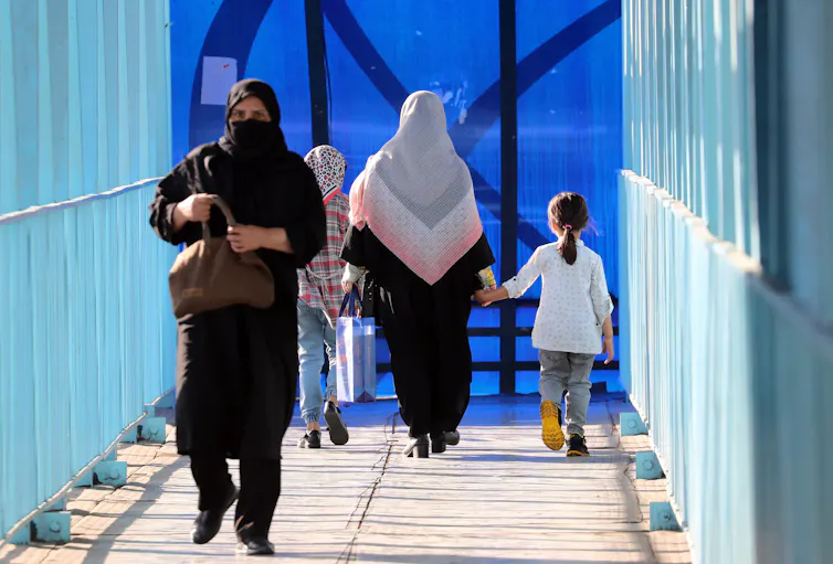 Women and girls walk on a pedestrian bridge in a street in Tehran wearing the compulsoty hijab.