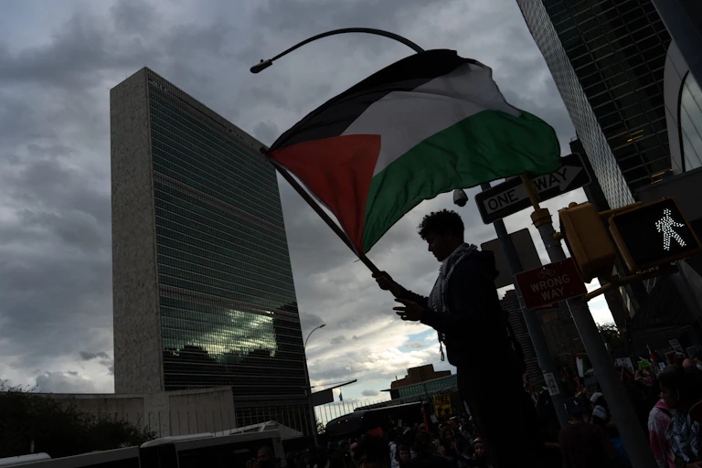 A person waves a Palestinian flag in front of a tall building.
