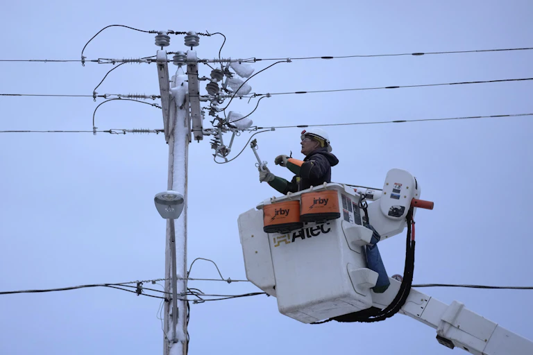 A bucket truck raises a lineman toward a power pole.