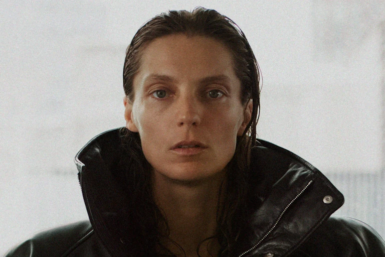 A woman with slicked back hair and a black shiny jacket.
