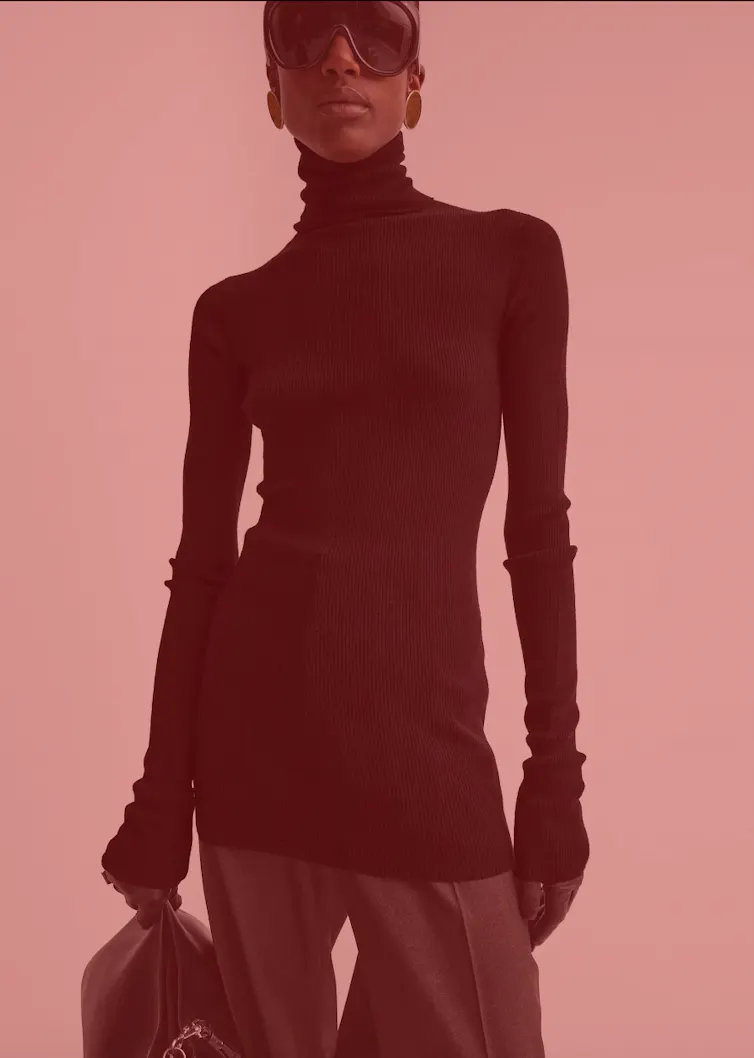 A black model dressed in black in black sunglasses against a pale red background.