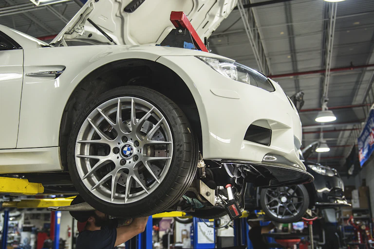 a person reaching up underneath a car that is raised on a lift in a garage