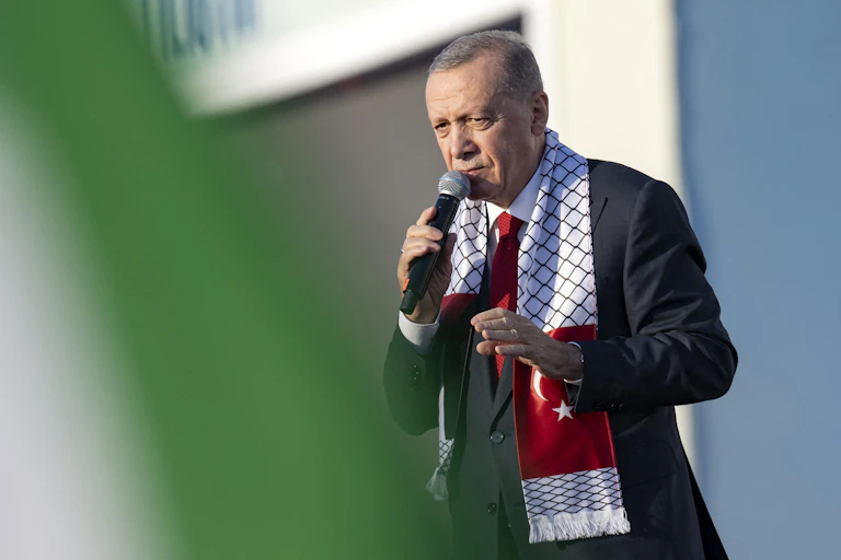 A man draped in a scarf talks into a microphone.