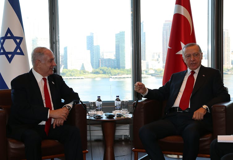 Two men in suits and red ties sit at a table.