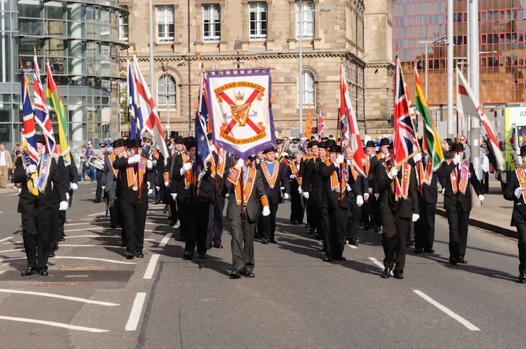 Orange Order men marching in Northern Ireland wearing bowler hats and carrying banners.