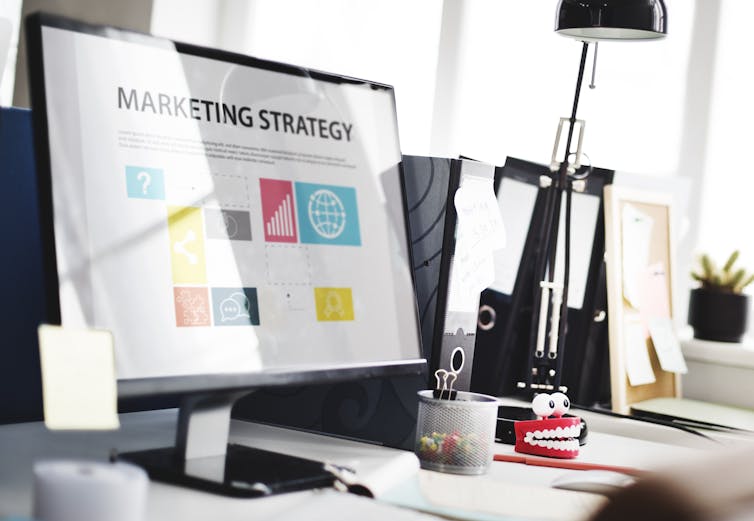 A computer screen on a desk displaying the phrase 'marketing strategy' along with colourful square icons