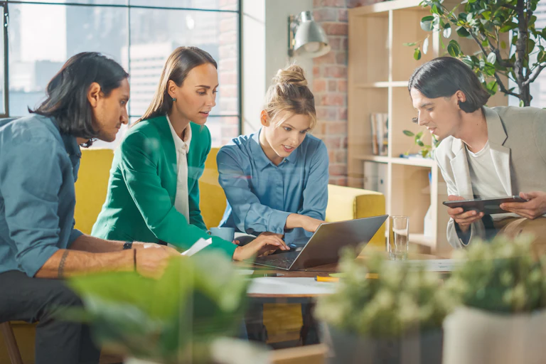 A group of people sitting around a coffee table and looking at an open laptop sitting on top of it