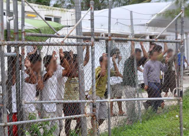 A row of men behind a wire fence at a detention centre.