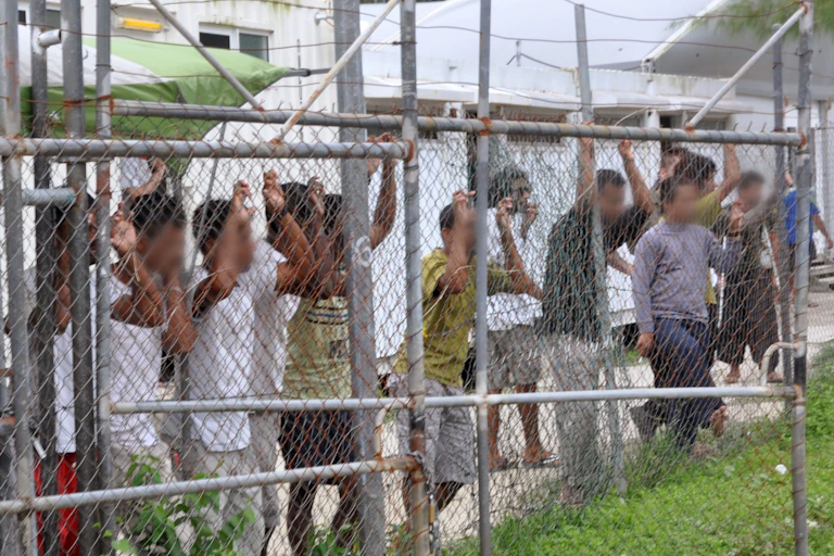 A row of men behind a wire fence at a detention centre.