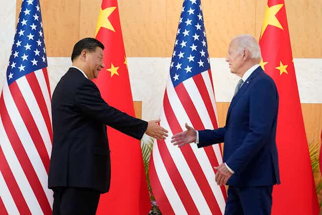President Xi and president Xi meet at the G20 summit, shake hands in front of their flags.