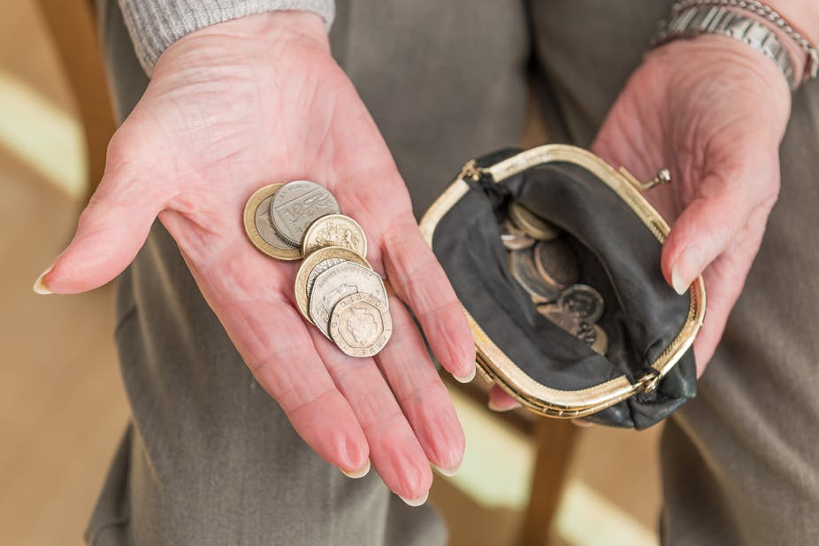 Hands of an elderly woman with British money in the palm of her hand and an open purse containing coins.