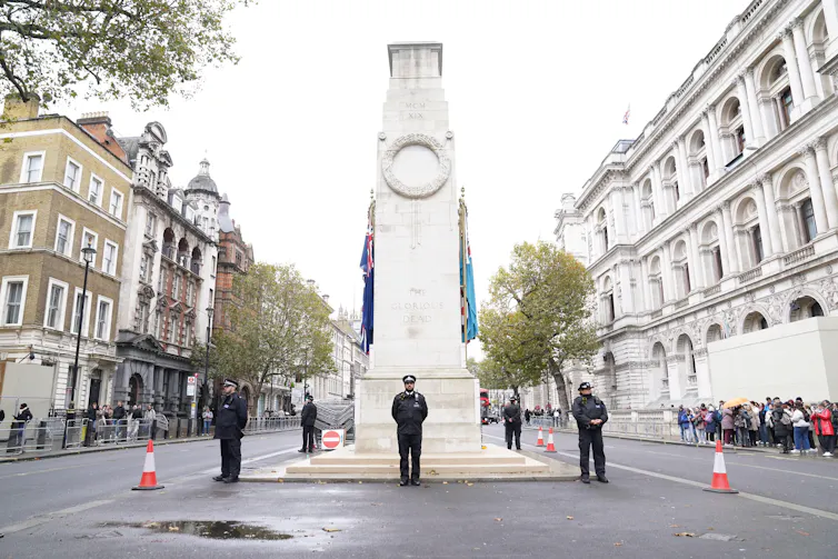 Policemen stand guard around a war memorial on an empty street.
