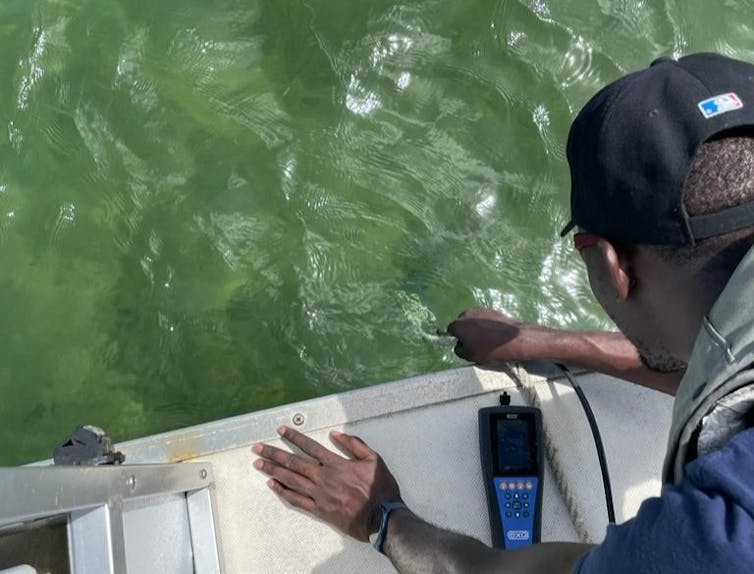 A man leans over the edge of a boat holding a rope attached to sampling devices that are in the water below.