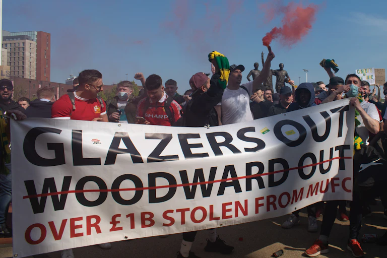 Manifestation de supporters brandissant des fumigènes et une pancarte « Glazers Out, Woodward out »