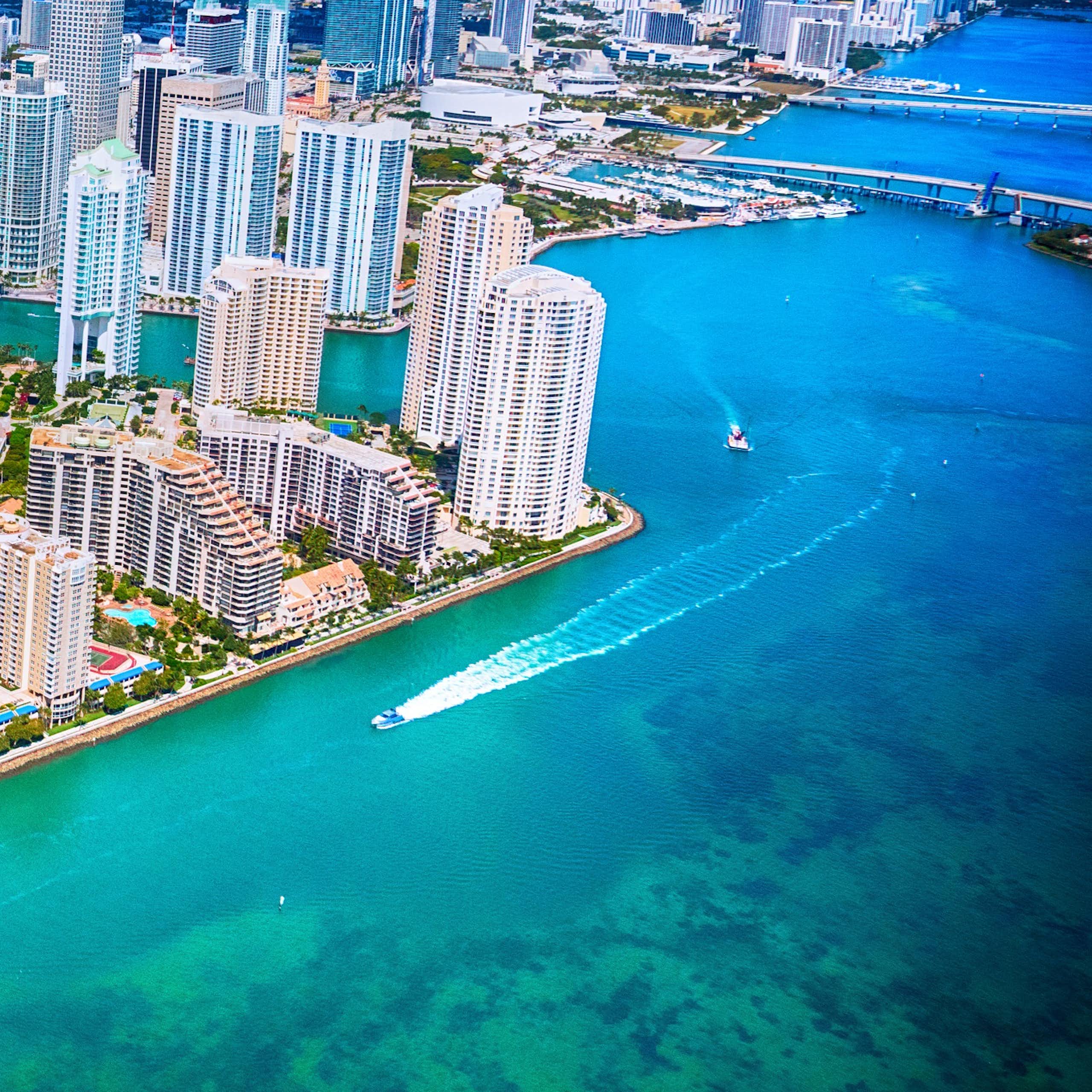 A helicopter of view of Miami's gleaming office towers over Biscayne Bay, where boats are running through the channels.