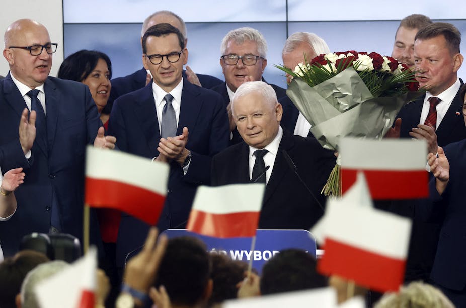 Plusieurs personnes sur une estrade devant un public brandissant des drapeaux polonais