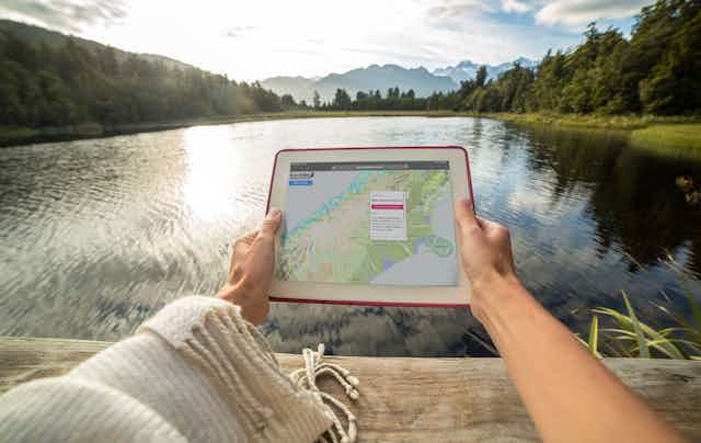 Someone at a lake or river, holding a digital device with the Eco index restoration map showing.
