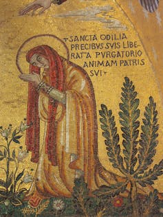 A painting of Saint Odile, bowing in a gold robe, among greenery