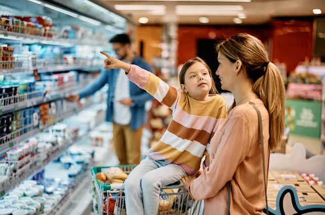 A child with her mother at the supermarket pointing to an item on the shelf.