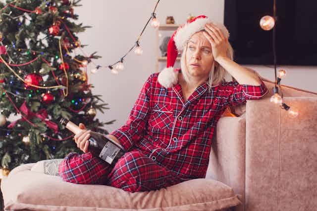 woman sits on couch looking tired with christmas tree nearby