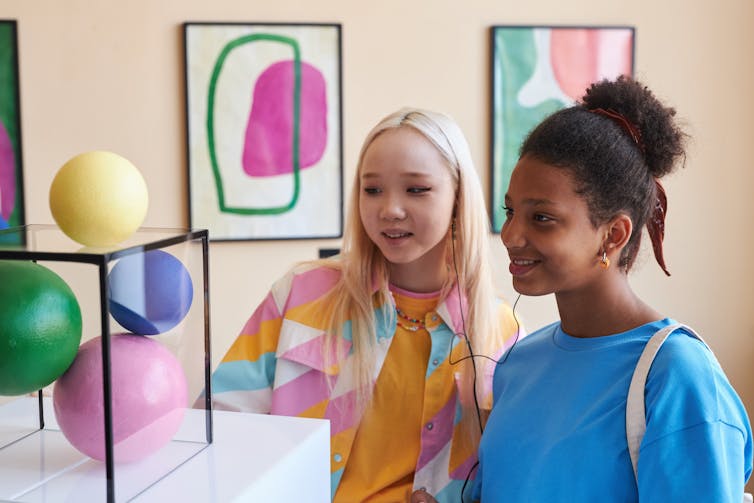 Two teenage girls look at art.
