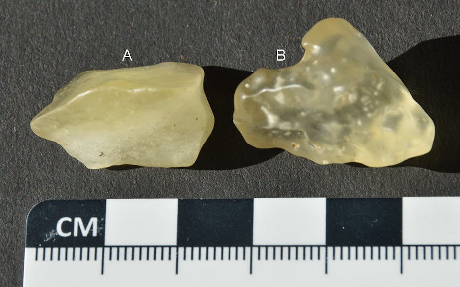 A photograph of two yellow stones - one appears almost translucent and the other is a deeper yellow - against a black background, with a small ruler beneath them for scale