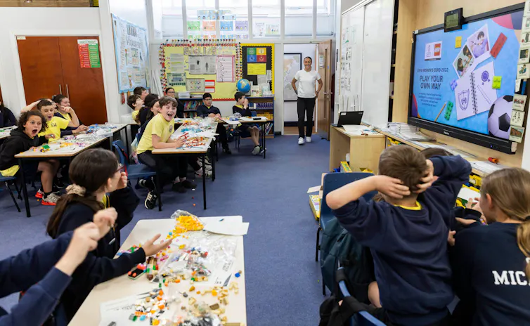 Children in yellow and blue school uniforms work in a classroom.