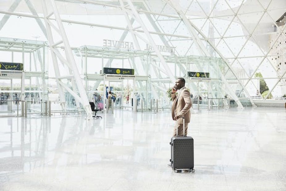 Plan large d'un homme portant un costume, debout avec une valise et utilisant un téléphone dans un terminal d'aéroport.