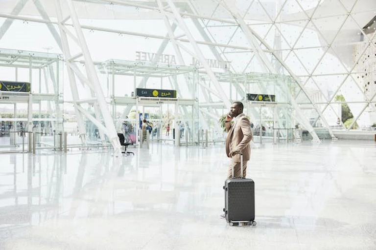 Plan large d'un homme portant un costume, debout avec une valise et utilisant un téléphone dans un terminal d'aéroport.