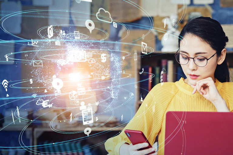 Woman using laptop and phone with location and other data-related icons.