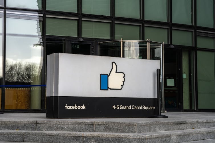 A thumbs up sign with the words facebook and 4-5 Grand Canal Quay, in front of a glass office building.