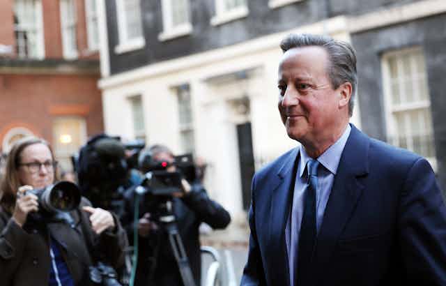 David Cameron walking in Downing Street in front of media photographers.