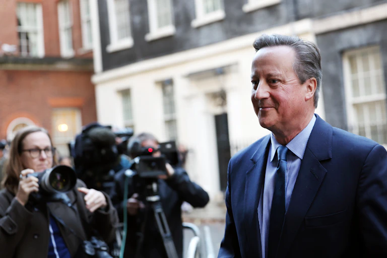 David Cameron walking in Downing Street in front of media photographers.