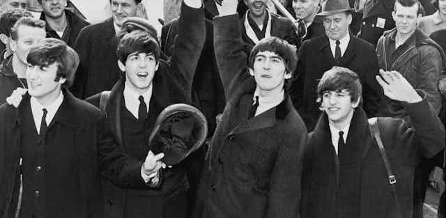 black and white photo of the Beatles waving to fans.