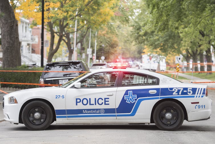 A police cruiser sits at the end of a street with police tape behind it.