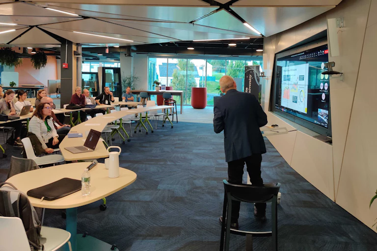 people at tables watching a presenter by a screen