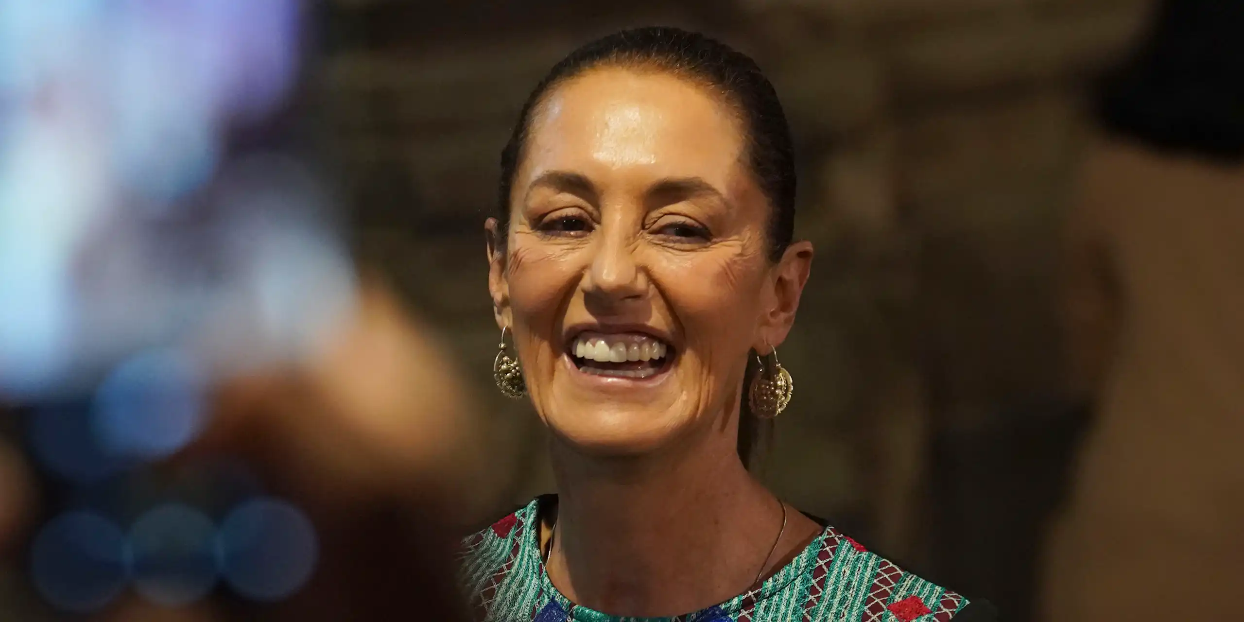 Una mujer con un top de colores y pendientes de lazo sonríe.