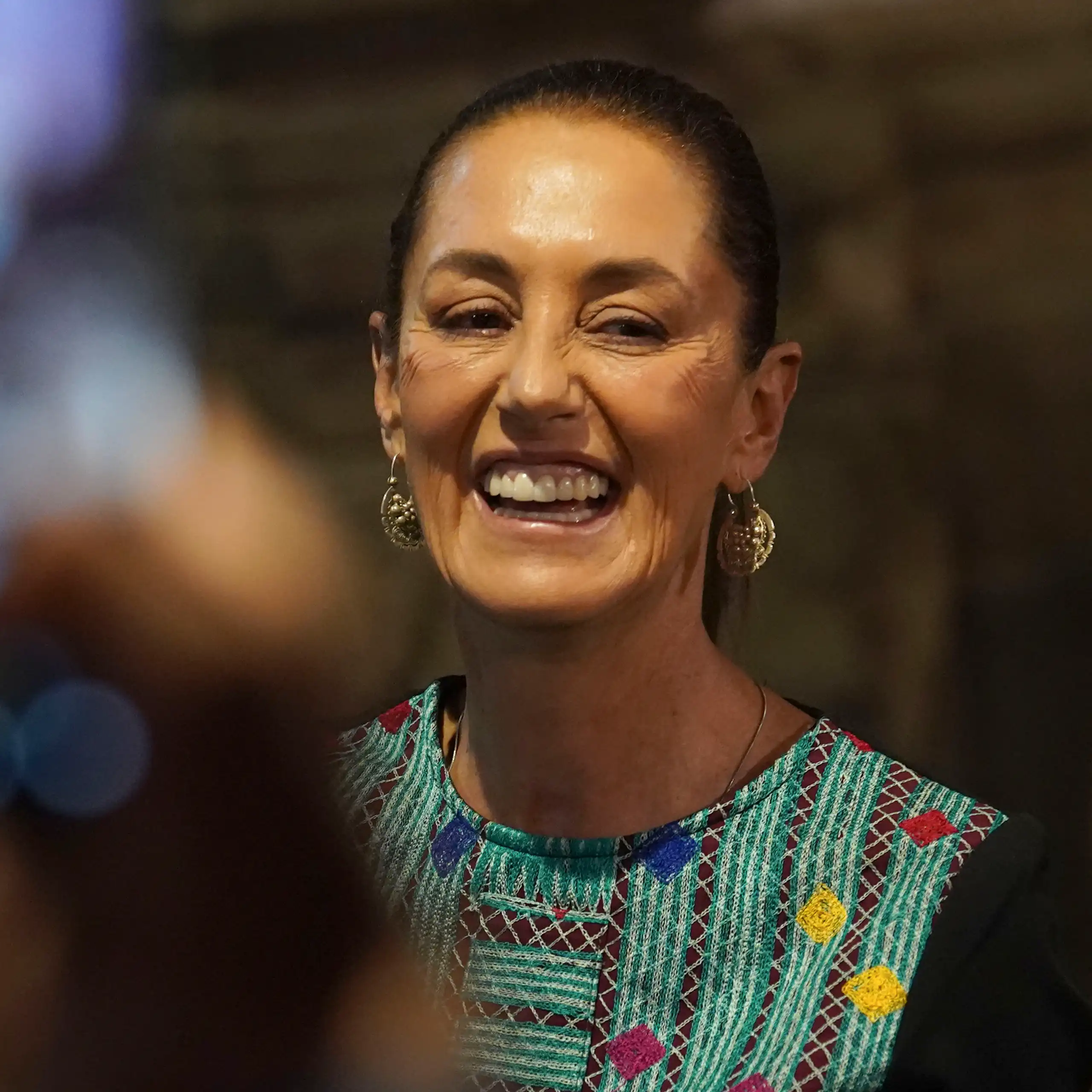 Una mujer con un top de colores y pendientes de lazo sonríe.
