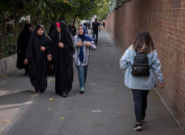 The back of a woman without a headscarf is seen walking toward a group of women all veiled.
