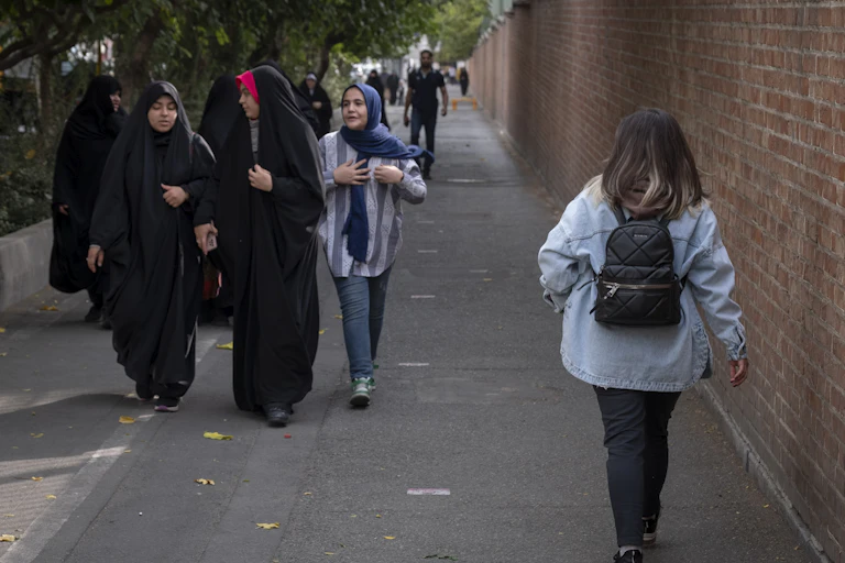 The back of a woman without a headscarf is seen walking toward a group of women all veiled.