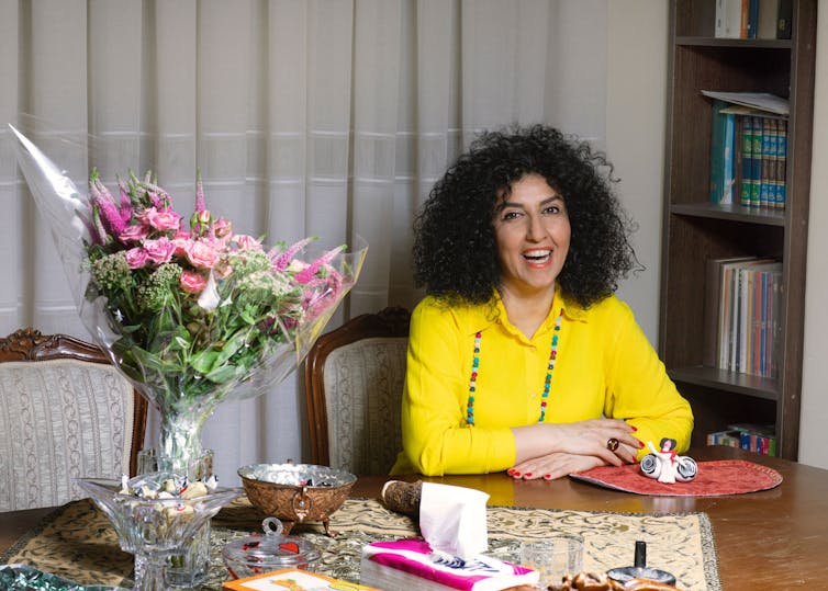 Narges Mohammadi wears a yellow shirt and has a big smile as she sits at a table with flowers.