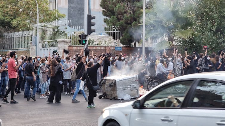 People march in the streets near a tipped over bin that appears on fire or is smoking.