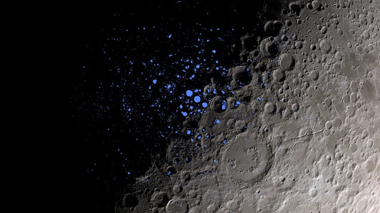 A close-up shot of the Moon's surface, with the left half covered in shadow, and the right half visible, with gray craters. Tiny blue dots in the center indicate PSRs.