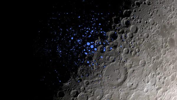 A close-up shot of the Moon's surface, with the left half covered in shadow, and the right half visible, with gray craters. Tiny blue dots in the center indicate permanently shadowed regions.
